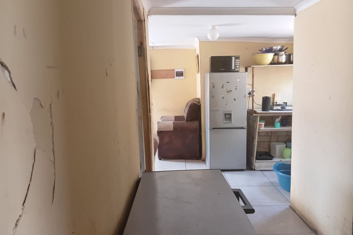 A view into a kitchen area showing tiled floors and built-in shelving, currently requiring maintenance and cosmetic updates to the wall finishes.