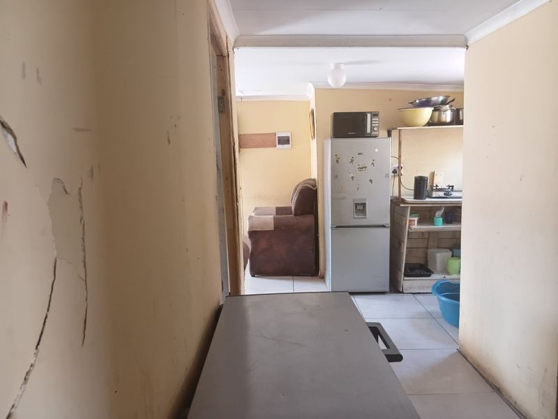 A view into a kitchen area showing tiled floors and built-in shelving, currently requiring maintenance and cosmetic updates to the wall finishes.