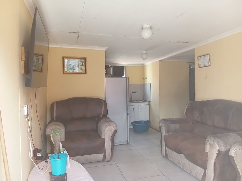 Open plan living area featuring tiled flooring and a compact kitchen corner with sink and cabinetry, showing signs of wear and ceiling damage.