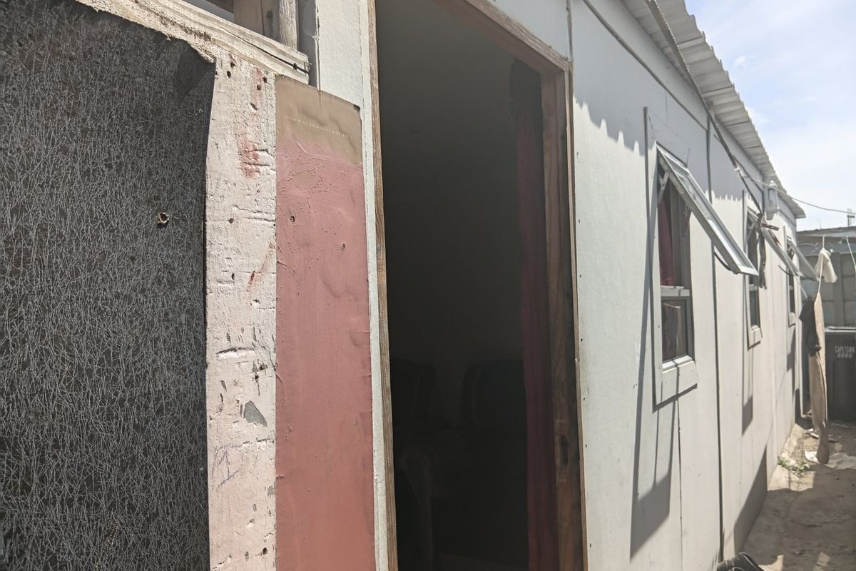 Exterior view of a structure showing weathered wall cladding, corrugated metal roofing, and basic casement windows.