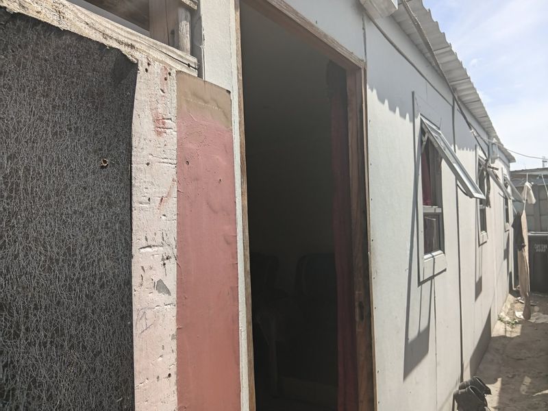 Exterior view of a structure showing weathered wall cladding, corrugated metal roofing, and basic casement windows.