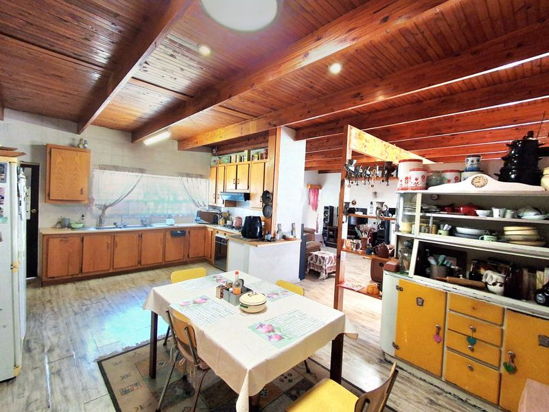 Spacious open-plan kitchen and dining area featuring exposed timber beam ceilings, extensive wooden cabinetry, and integrated cooking appliances.