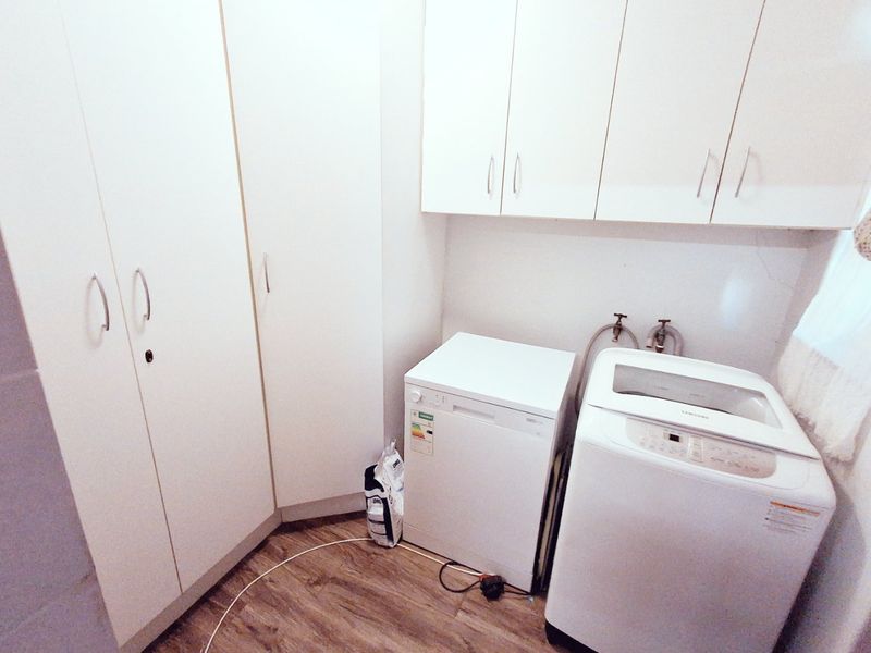 A functional laundry room featuring built-in white cabinetry, dedicated plumbing connections, and durable laminate flooring.