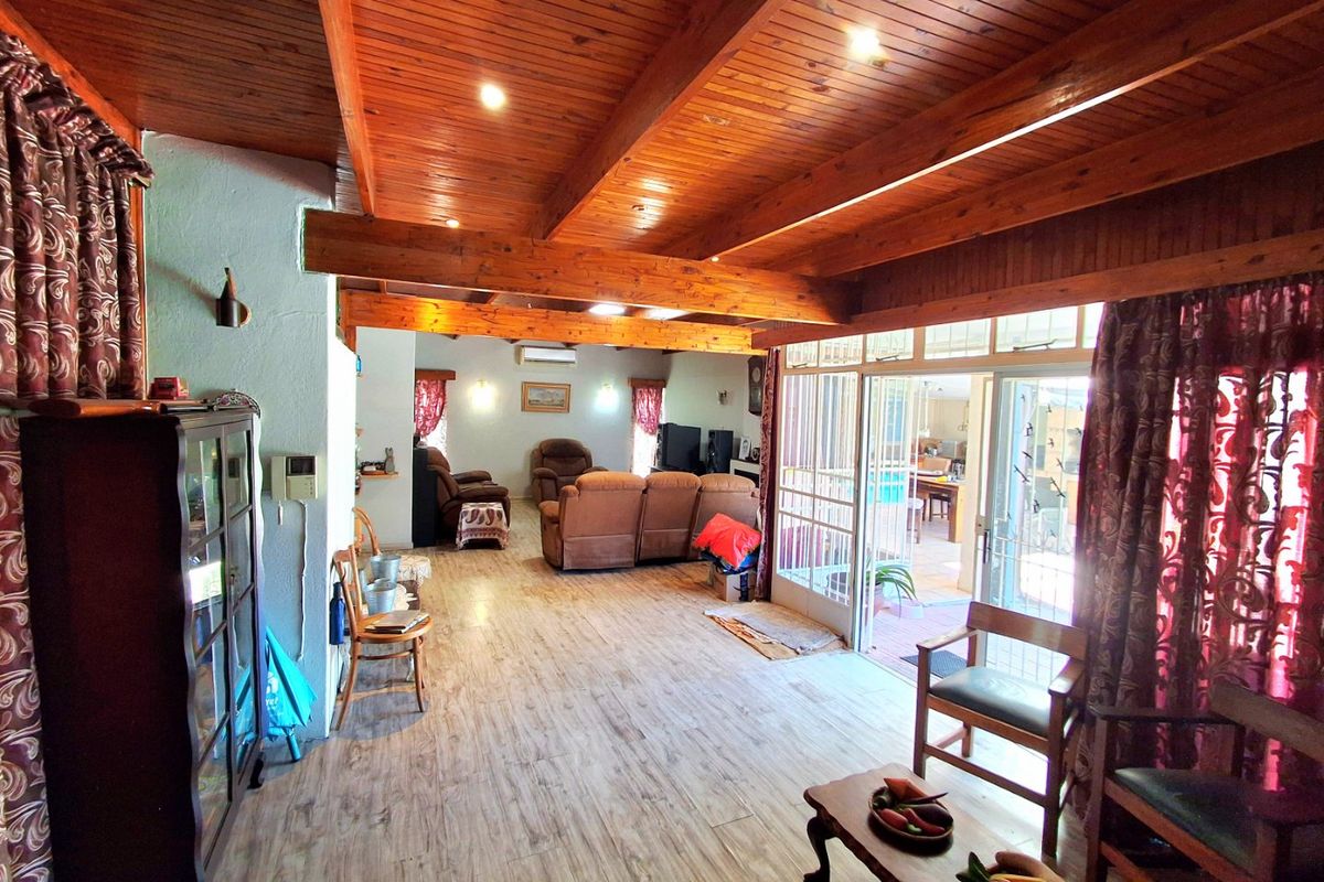 Spacious living area featuring exposed timber ceiling beams, wood-look laminate flooring, and large sliding glass doors providing access to the outdoor patio area.
