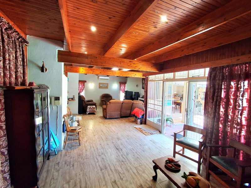 Spacious living area featuring exposed timber ceiling beams, wood-look laminate flooring, and large sliding glass doors providing access to the outdoor patio area.