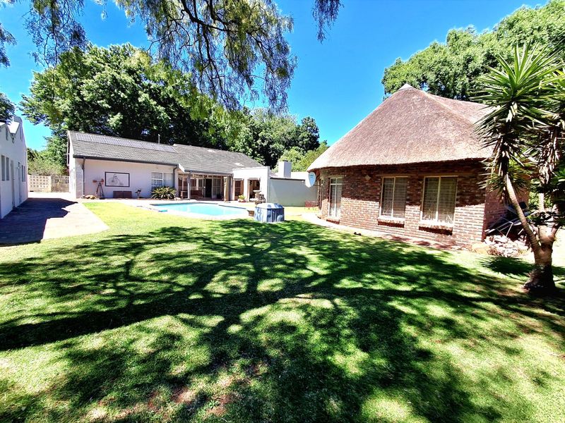 Spacious rear garden featuring a swimming pool, a brick-built structure with a traditional thatched roof, and a well-maintained lawn area.