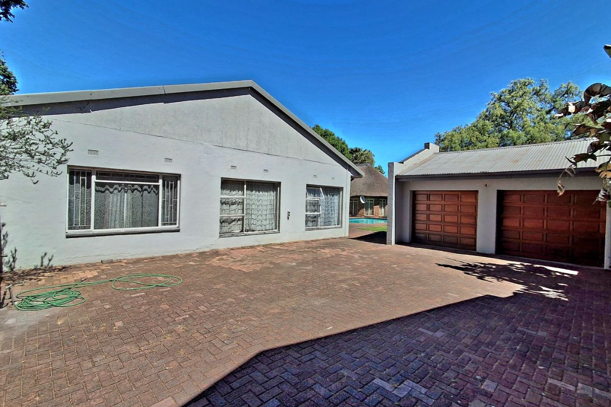 Rear view of the property featuring a spacious paved courtyard, double garage with timber doors, and access to the garden and pool area.