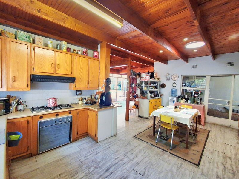 Open-plan kitchen and dining area featuring exposed timber beam ceilings, wooden cabinetry, and a gas hob, offering a functional layout with potential for modernization.