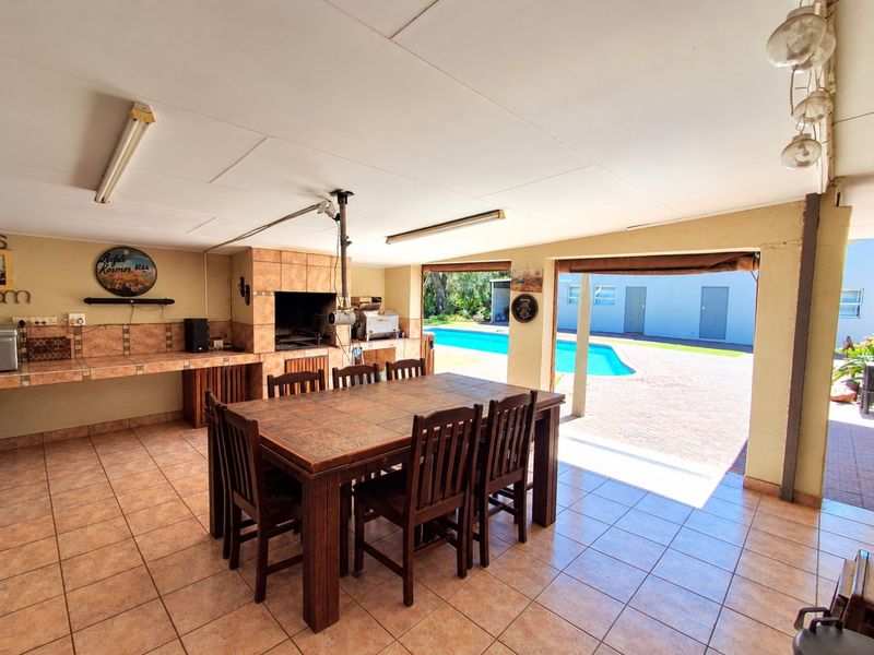Covered outdoor patio featuring a built-in braai area, tiled flooring, and direct access to the swimming pool and paved backyard.