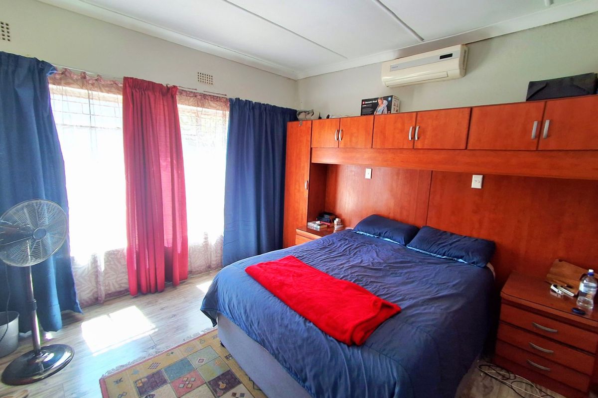 A bedroom featuring built-in wooden cupboards, laminate flooring, and a wall-mounted air conditioning unit.