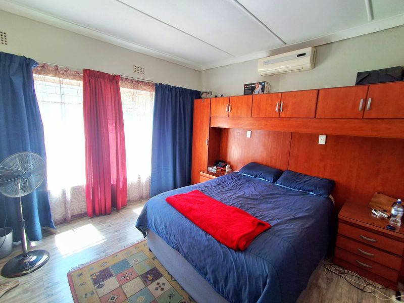 A bedroom featuring built-in wooden cupboards, laminate flooring, and a wall-mounted air conditioning unit.