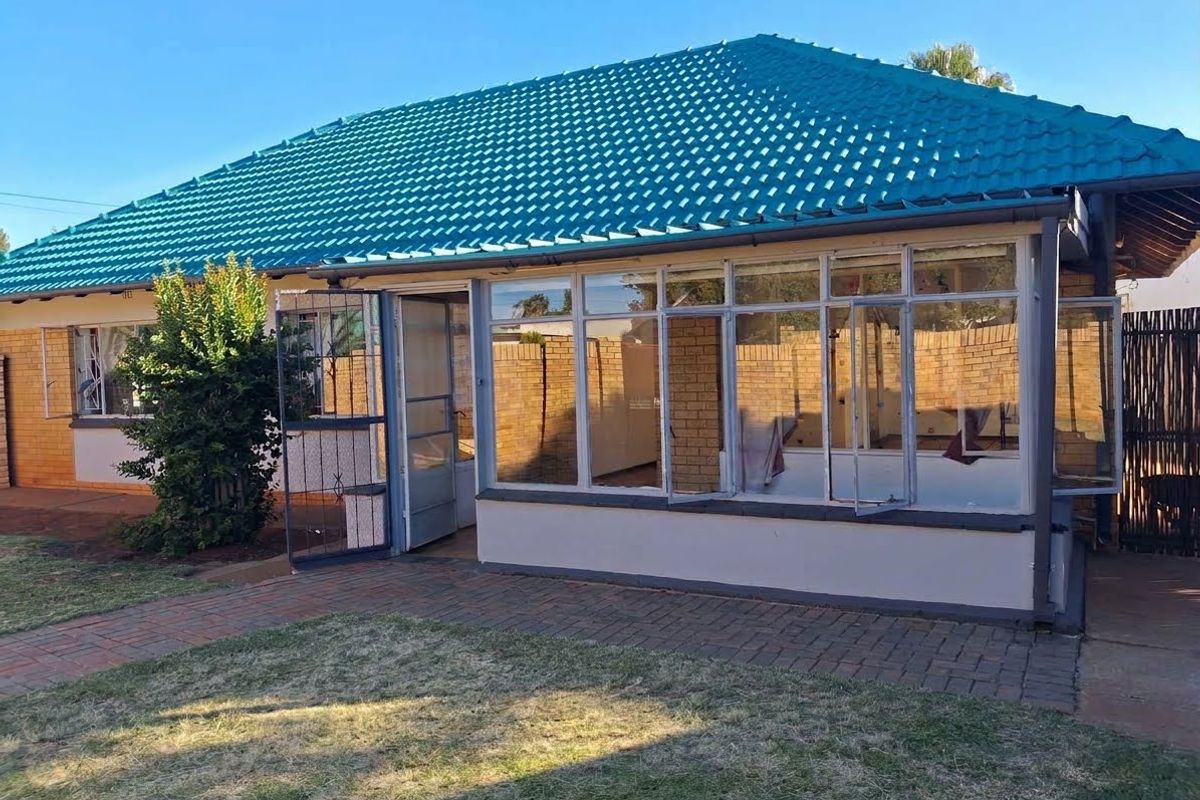 Rear view of the property featuring a tiled roof, brick exterior, and an enclosed patio area with a paved walkway leading to the entrance.