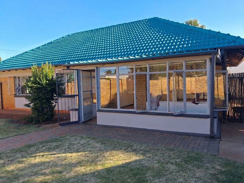 Rear view of the property featuring a tiled roof, brick exterior, and an enclosed patio area with a paved walkway leading to the entrance.