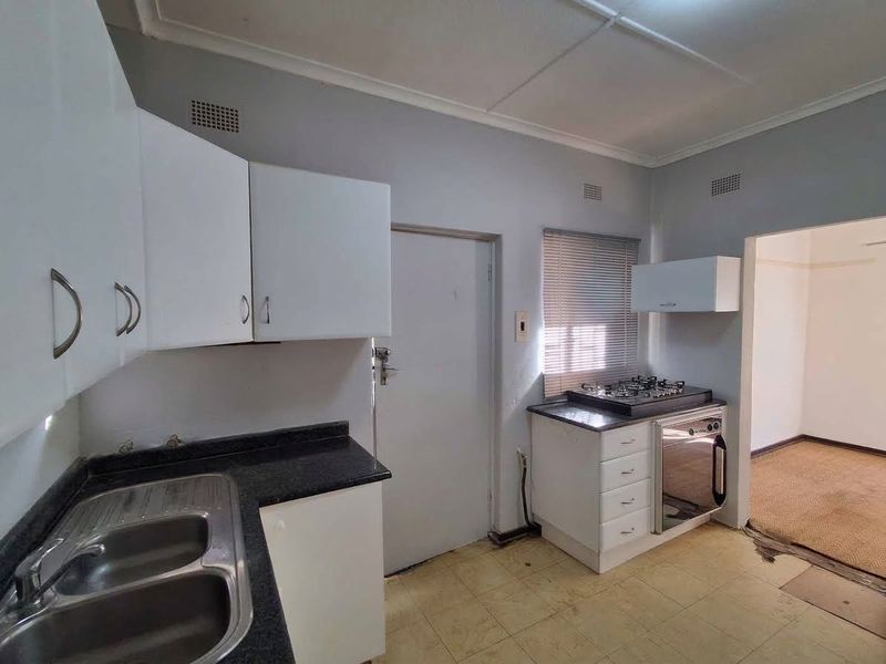 A functional kitchen featuring white cabinetry, a gas hob, built-in oven, and double bowl sink, requiring cosmetic updates to the flooring and finishes.
