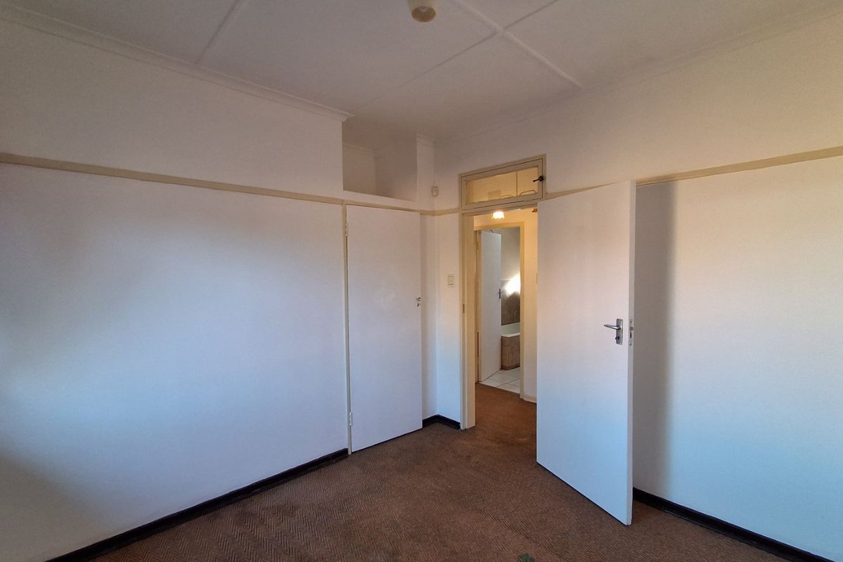 An empty bedroom featuring built-in cupboards, picture rails, and carpeted flooring, with a doorway leading to an adjacent room.