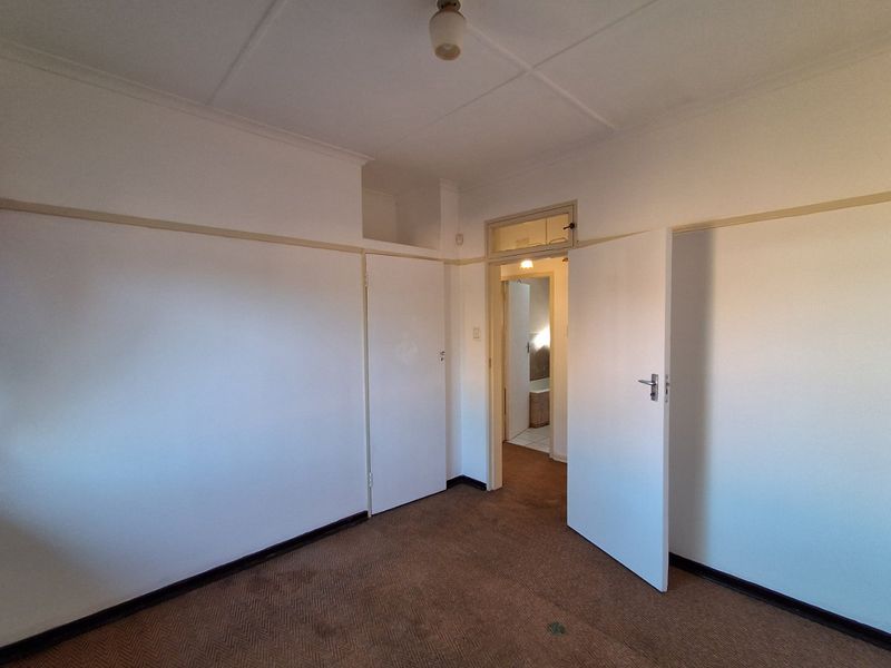 An empty bedroom featuring built-in cupboards, picture rails, and carpeted flooring, with a doorway leading to an adjacent room.