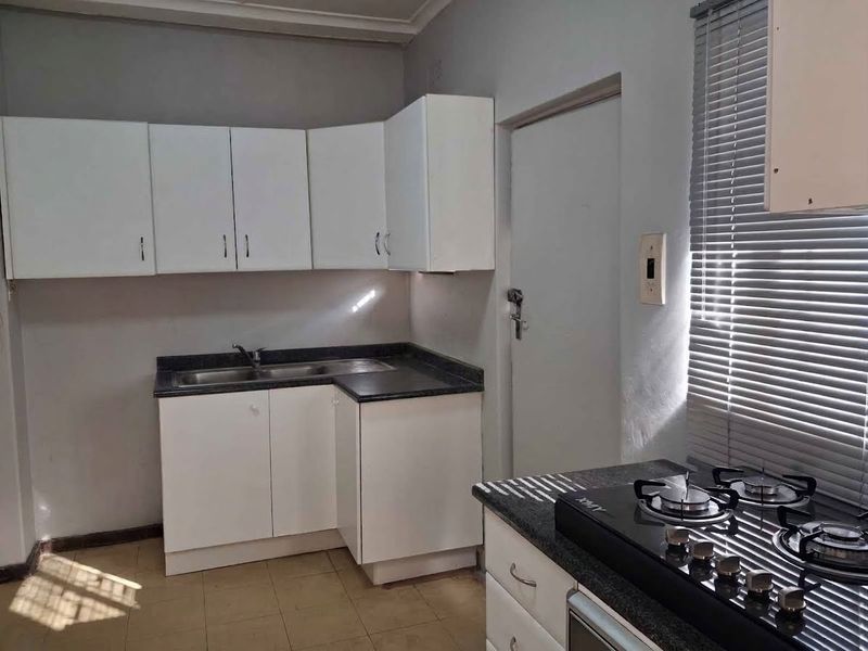A functional kitchen featuring white built-in cabinetry, dark laminate countertops, a stainless steel double sink, and a built-in gas hob.