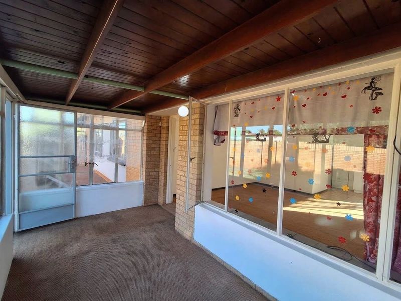 Enclosed patio area featuring a timber ceiling, brick wall accents, and large glass windows looking into the interior living space.