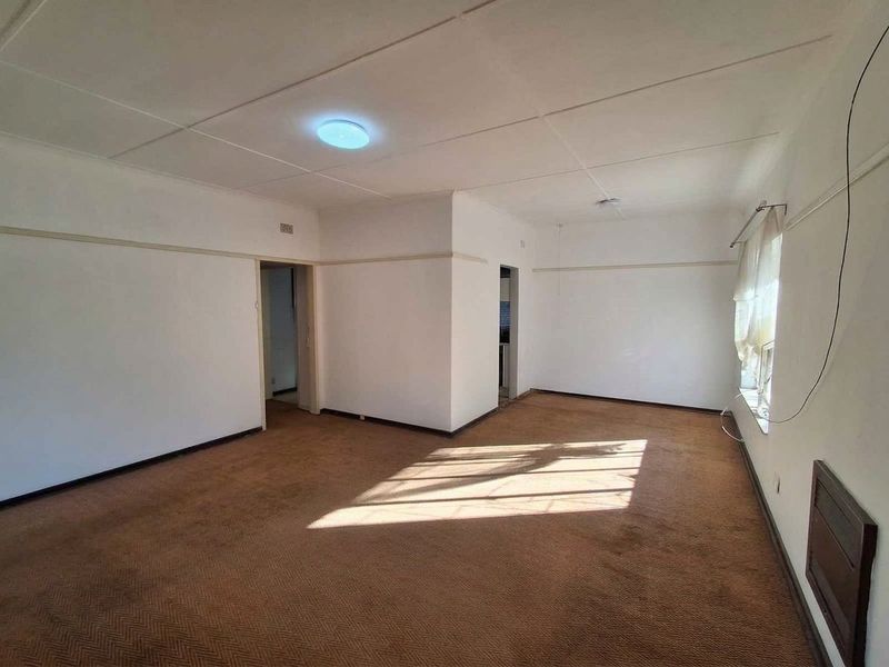 A spacious, empty living room featuring carpet flooring, ceiling tiles, and a picture rail, offering a blank canvas for renovation.