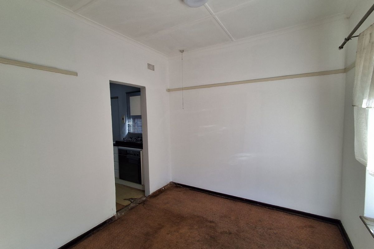 An empty living room featuring a picture rail and ceiling rose, with a view into the adjacent kitchen area.