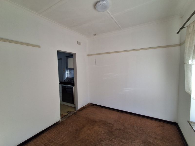 An empty living room featuring a picture rail and ceiling rose, with a view into the adjacent kitchen area.