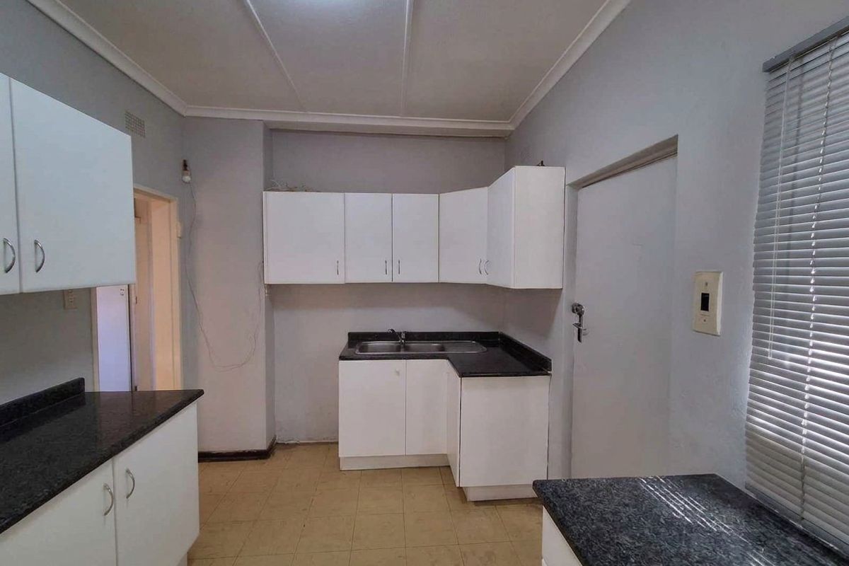 A functional kitchen featuring white built-in cabinetry, dark laminate countertops, a stainless steel sink, and tiled flooring, ready for a modern update.