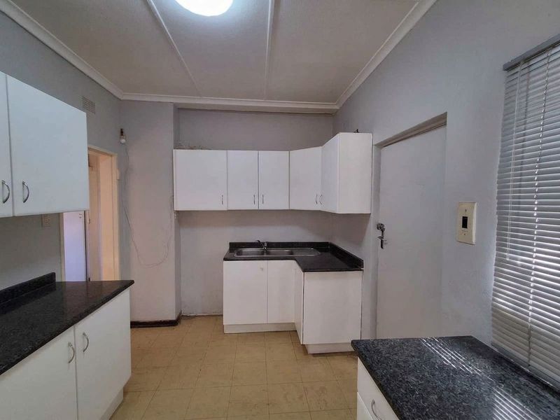 A functional kitchen featuring white built-in cabinetry, dark laminate countertops, a stainless steel sink, and tiled flooring, ready for a modern update.