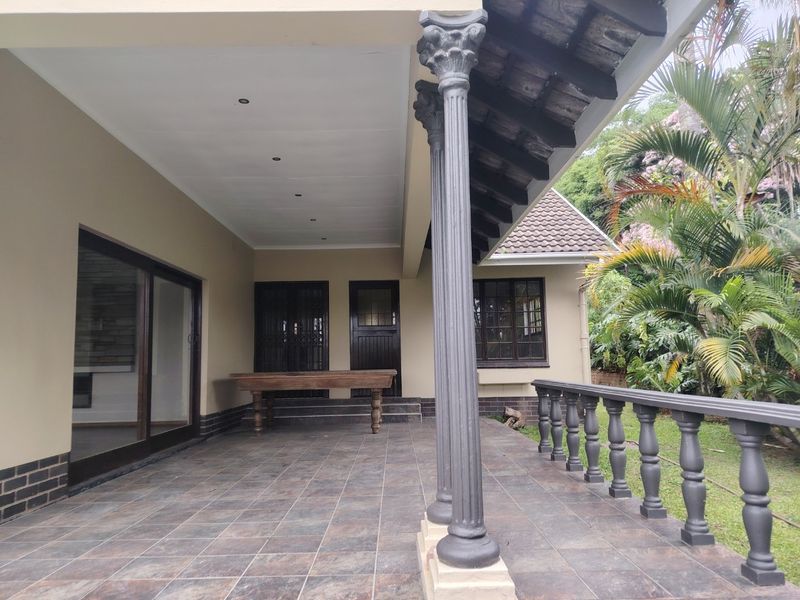A spacious covered patio featuring tiled flooring, decorative columns, and a balustrade, providing a seamless transition to the garden area.