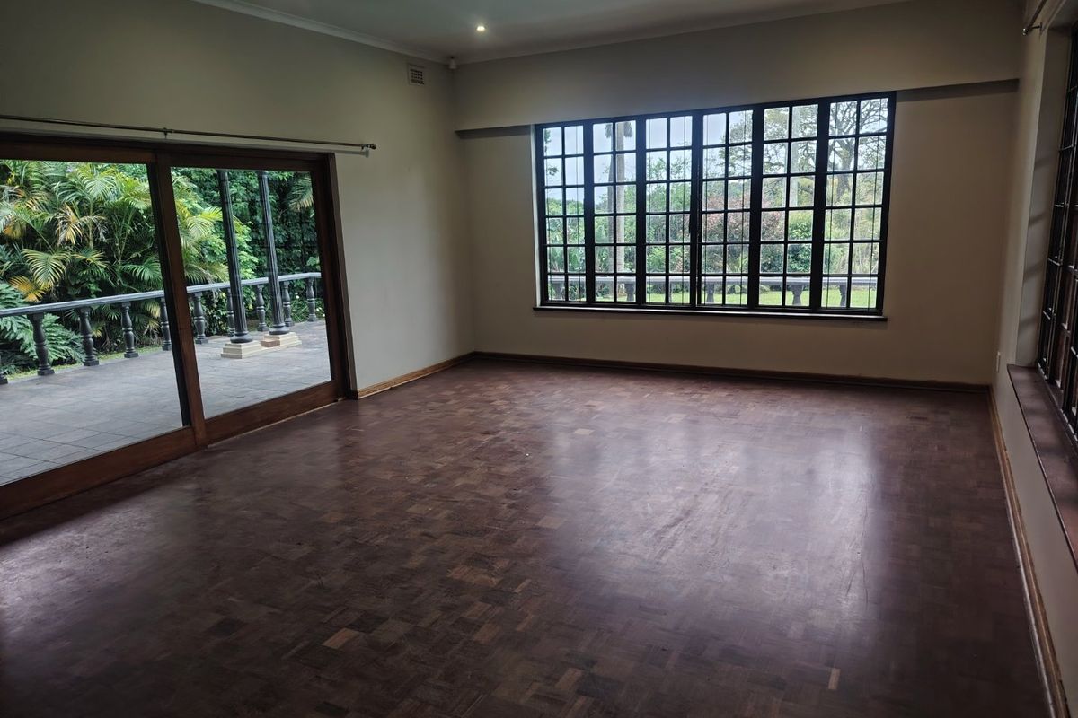 Spacious, empty living room featuring classic parquet flooring, large grid-pattern windows, and sliding glass doors that open onto an outdoor patio area.