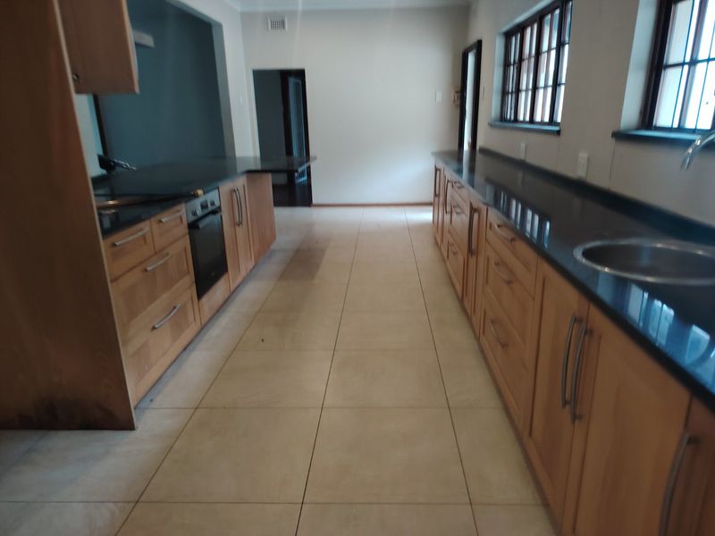 A galley-style kitchen featuring wooden cabinetry, dark granite countertops, built-in oven, and tiled flooring, offering a functional layout ready for personalization.