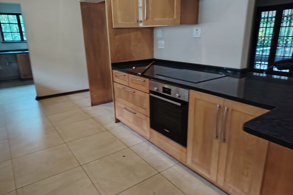 A functional kitchen featuring light wood cabinetry, black granite countertops, a built-in oven, and an electric hob, with neutral ceramic floor tiles throughout.