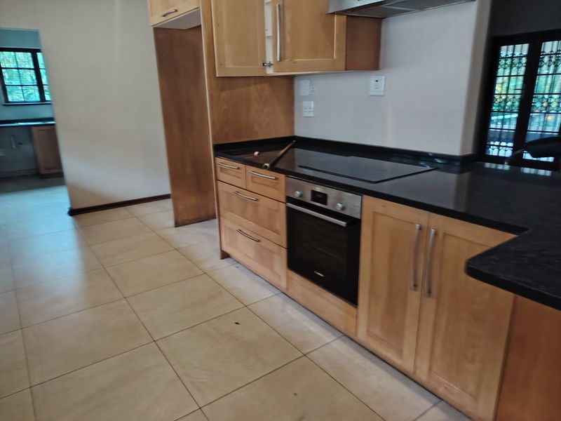 A functional kitchen featuring light wood cabinetry, black granite countertops, a built-in oven, and an electric hob, with neutral ceramic floor tiles throughout.