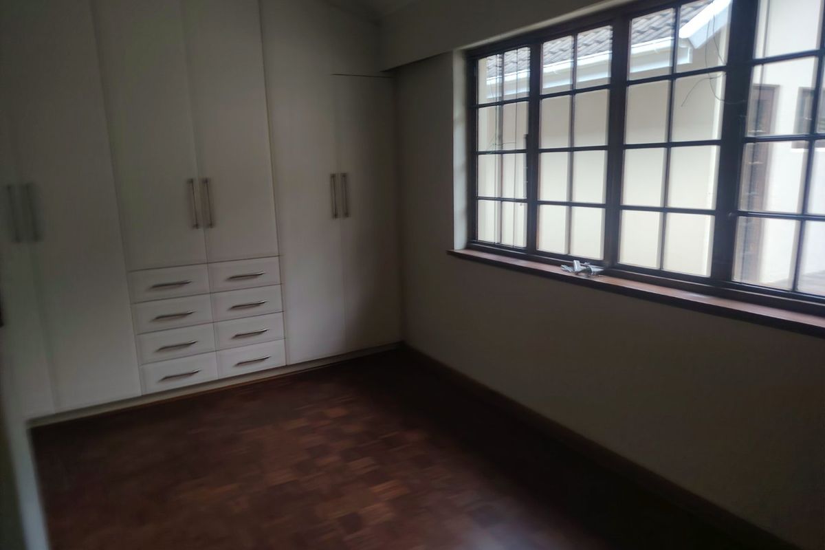 A bright, empty bedroom featuring classic parquet flooring and extensive built-in cupboard storage, offering a clean and versatile space.