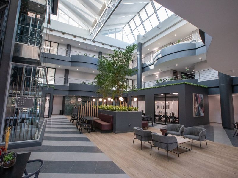 Modern commercial atrium featuring a multi-level mezzanine, expansive skylight, glass elevator, and integrated office spaces with contemporary finishes.