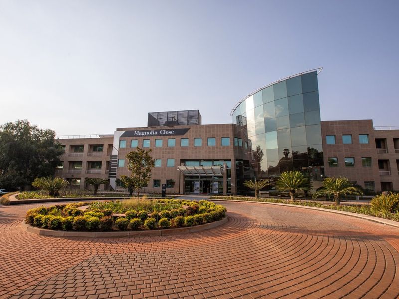 Professional exterior view of Magnolia Close commercial office building featuring a modern glass facade, paved circular driveway, and well-maintained landscaped grounds.