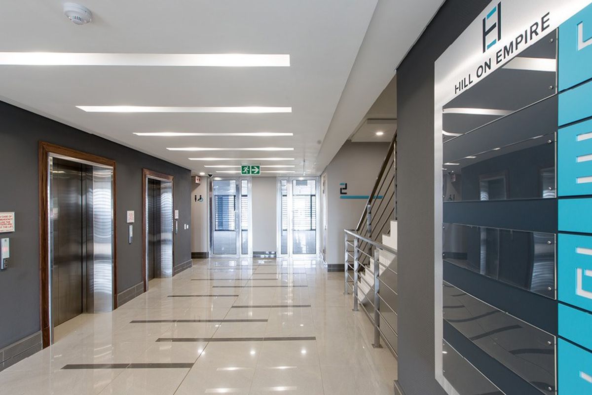 Modern commercial building hallway featuring polished tiled floors, recessed ceiling lighting, stainless steel elevator doors, and a directory board for Hill on Empire.