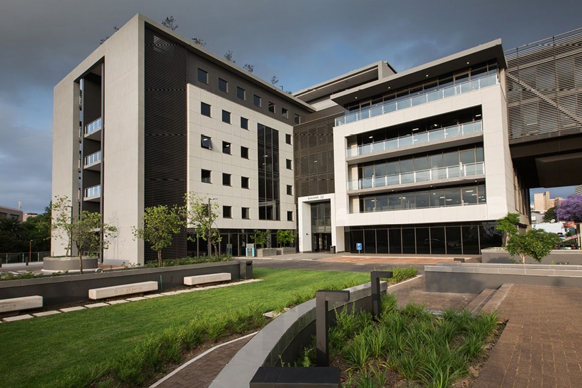 Modern commercial office building exterior featuring contemporary architectural design, glass balconies, and well-maintained landscaped grounds with paved pedestrian walkways.