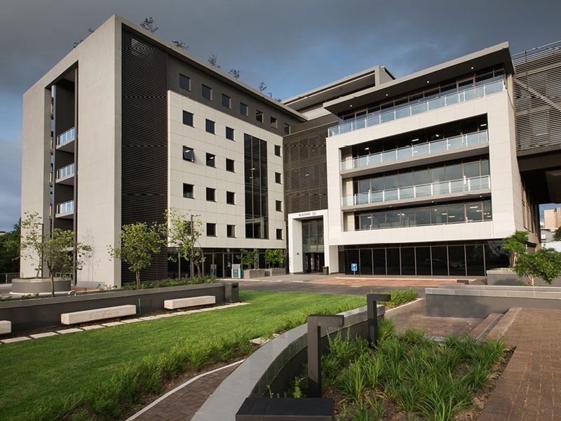 Modern commercial office building exterior featuring contemporary architectural design, glass balconies, and well-maintained landscaped grounds with paved pedestrian walkways.