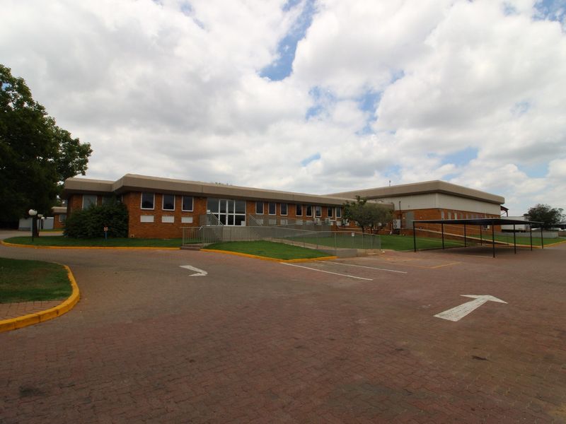 Front exterior view of an industrial office building featuring a brick facade, paved parking area, carport, and accessible ramp entrance.