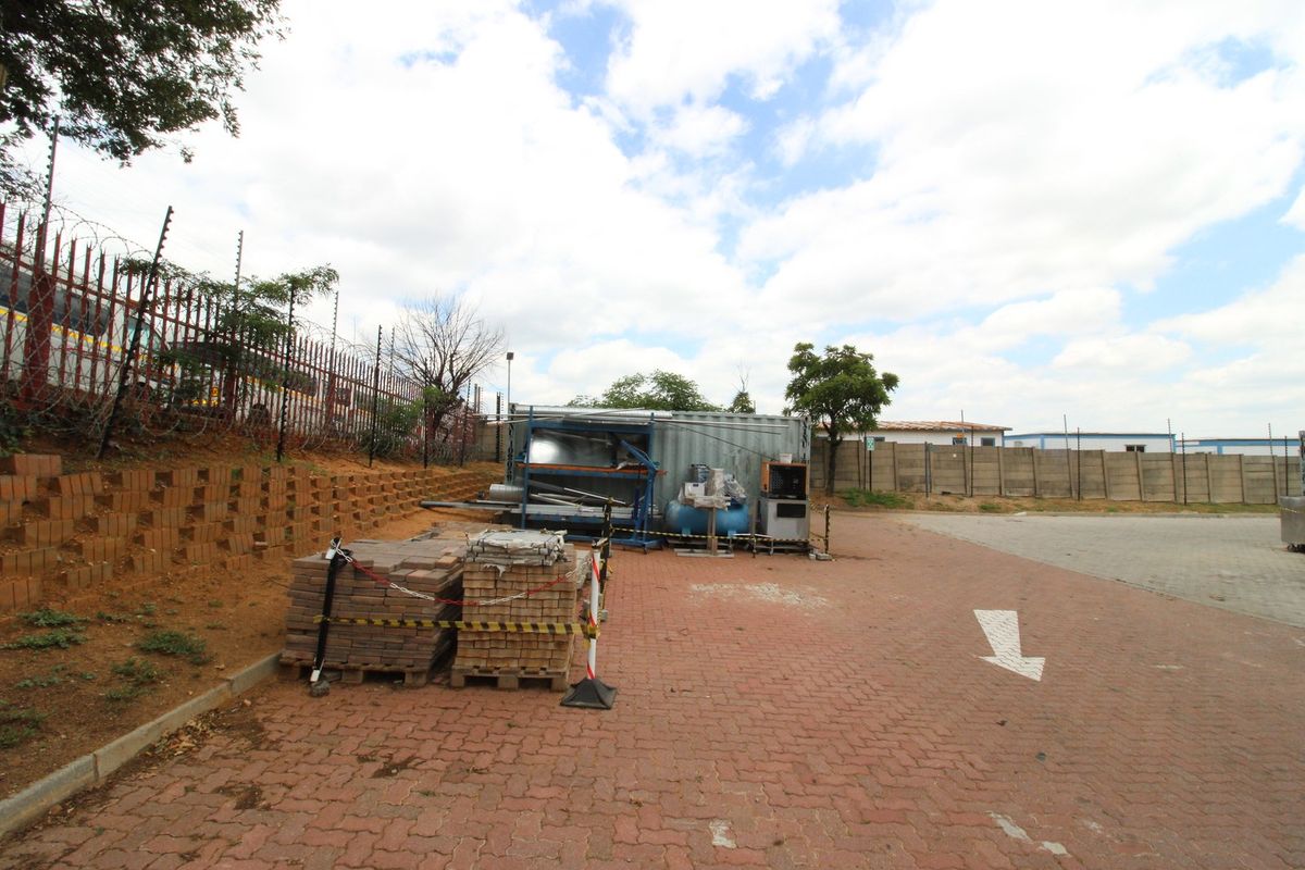 Industrial exterior yard area featuring paved surfacing, perimeter walling with electric fencing, and a retaining wall structure.