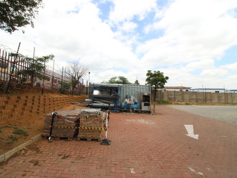 Industrial exterior yard area featuring paved surfacing, perimeter walling with electric fencing, and a retaining wall structure.