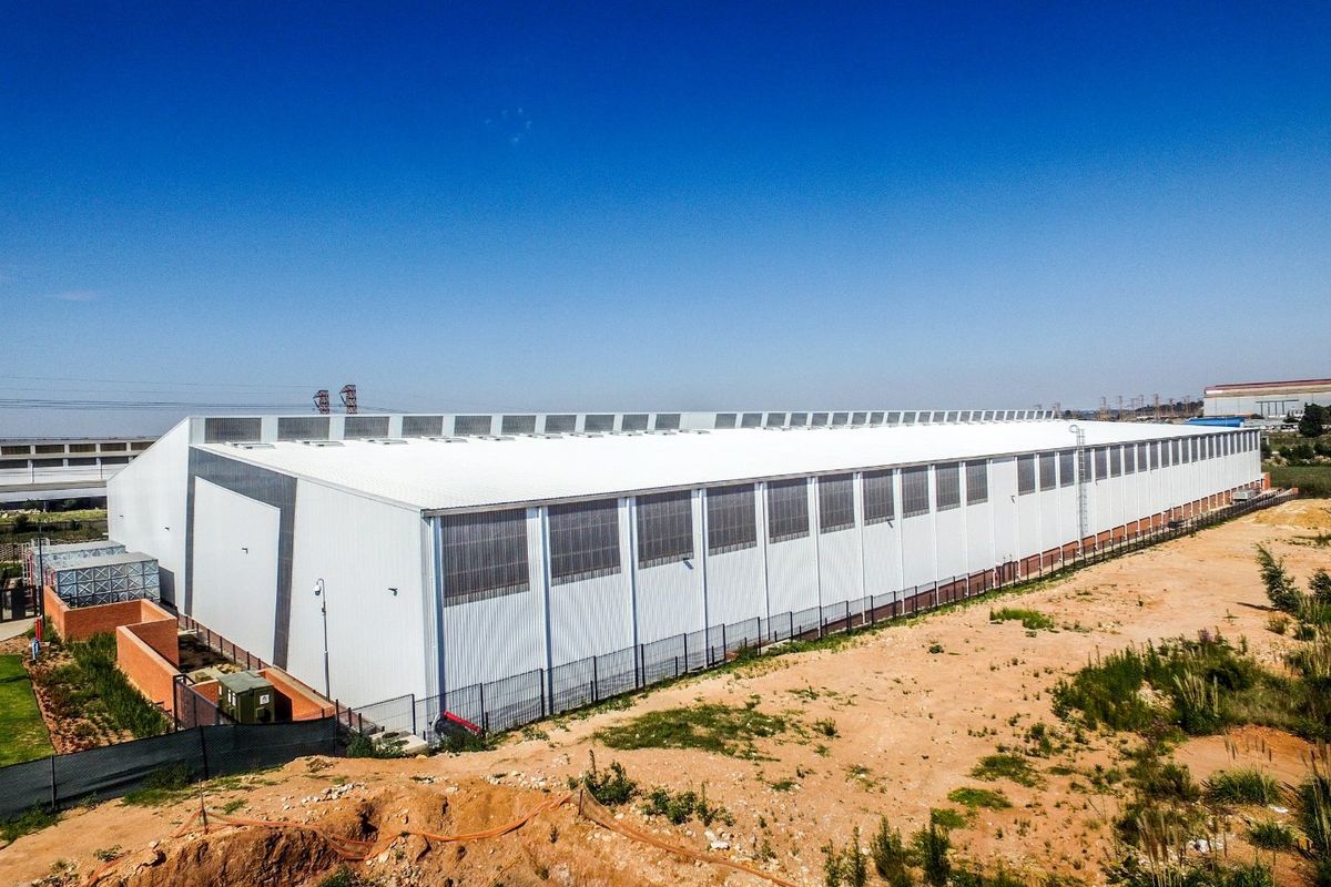 Aerial view of a large industrial warehouse facility featuring metal cladding, clerestory windows, and secure perimeter fencing on a spacious site.