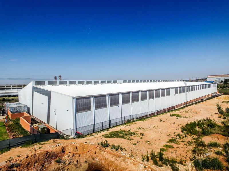 Aerial view of a large industrial warehouse facility featuring metal cladding, clerestory windows, and secure perimeter fencing on a spacious site.