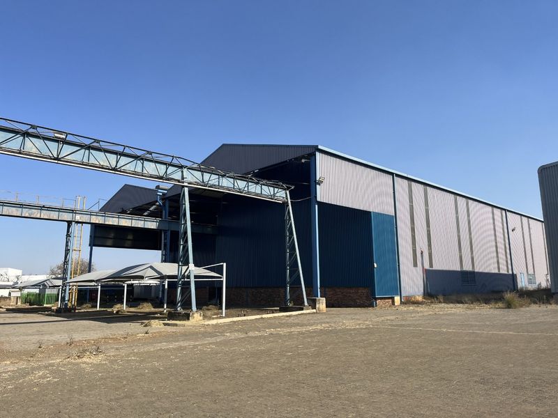 Industrial property featuring a large warehouse with metal cladding, an external steel gantry system, and a paved yard area.