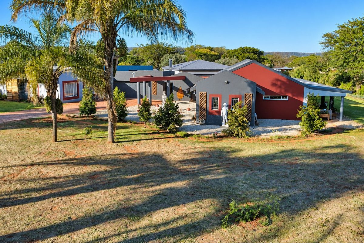 An elevated view of the rear exterior of the farm property, featuring a paved driveway, covered patio area, and landscaped grounds.