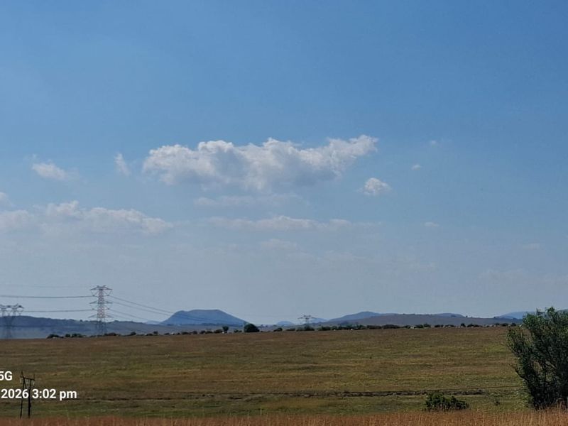 A wide-angle view of open, undeveloped residential land featuring distant hills and visible power line infrastructure.
