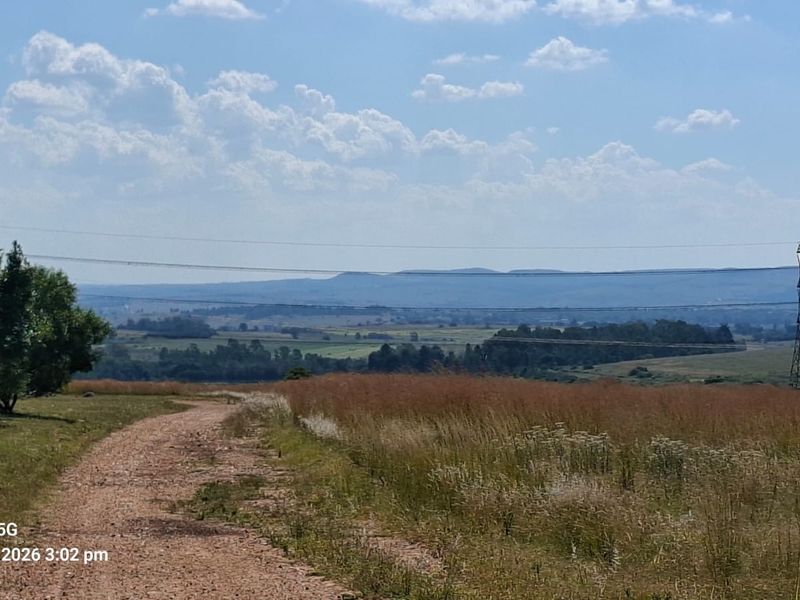 Expansive landscape view from the vacant residential property, featuring a dirt access track, natural grassland, and distant mountain vistas.