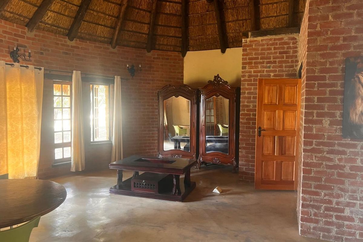 A rustic living area featuring exposed brick walls, a traditional thatched roof, and concrete flooring, offering a unique architectural aesthetic.