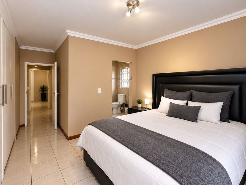 Spacious bedroom featuring tiled flooring, built-in cupboards, and an en-suite bathroom with neutral wall finishes.