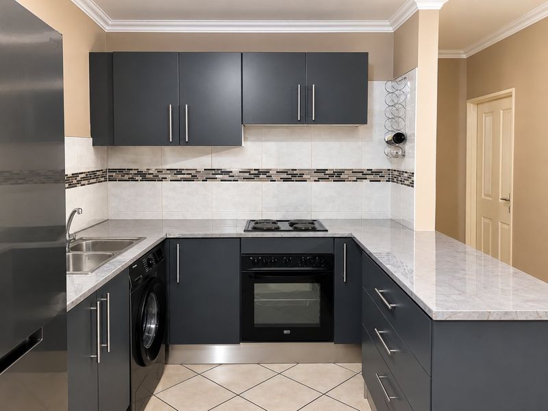 Modern kitchen featuring dark grey cabinetry, stone countertops, integrated oven and hob, tiled backsplash, and ceramic floor tiles.
